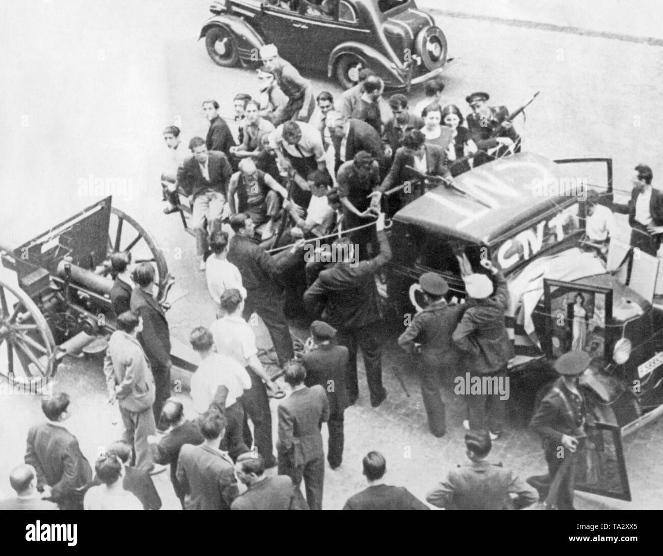 A partly armed unit of the anarcho-syndicalist Spanish trade union Confederacion Nacional del Trabajo (CNT, written on the truck) and civilians are trying to recover a confiscated cannon with a leash on the street of a Spanish city during the Spanish Civil War. In the background, an automobile. After the outbreak of the Civil War on June 17, 1936, many cities of Spain were the scene of street fights between Republicans, Communists and Nationalists. Stock Photo
