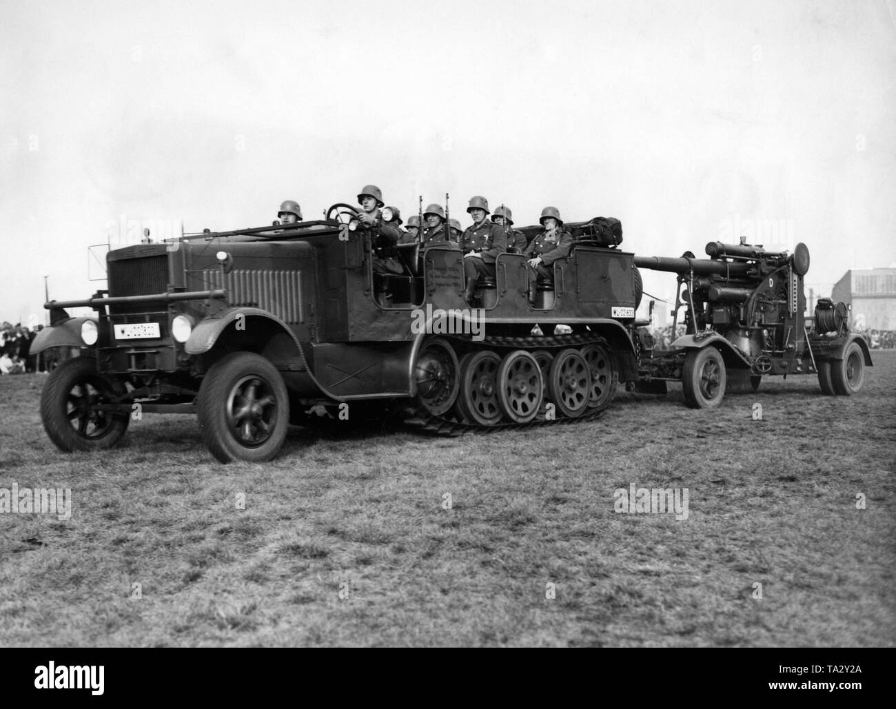 Maneuvers during the first major air show of the Luftwaffe in Staaken in favor of the Winter Relief. The picture shows soldiers in a Sd.Kfz. 6, which pulls an 8.8 cm Flak 18. In the background, crowds of spectators. Stock Photo