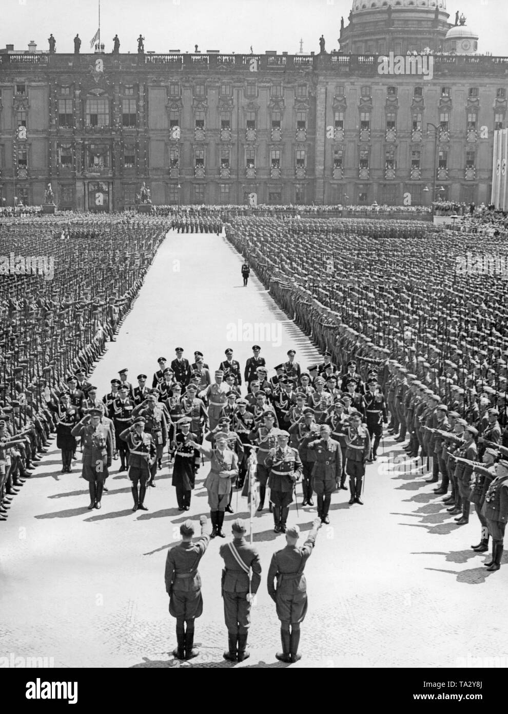 Photo of three officers of a delegation of the Condor Legion (front), who are greeting leader Adolf Hitler (first row left), Field Marshal General Hermann Goering (next on the right), the commander of the Legion, Major General Wolfram Freiherr von Richthofen (behind, on the right) and their entourage in the Lustgarten in front of the Berlin Palace. On the right and on the left, soldiers of the Condor Legion have lined up. Stock Photo