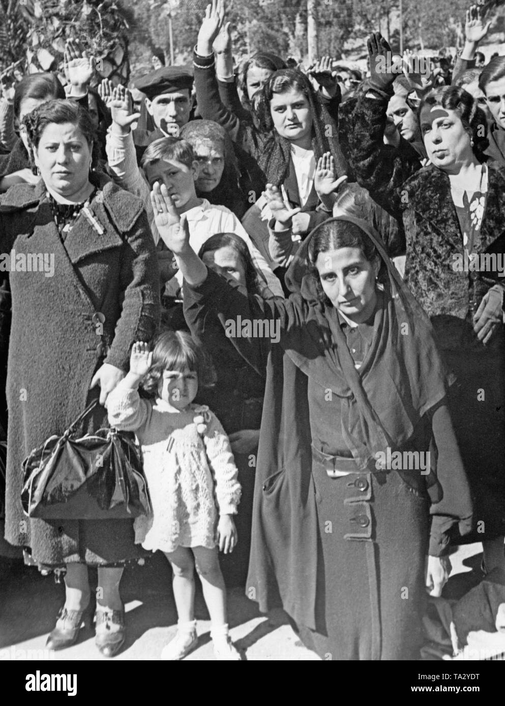 Women and children give the Fascist salute to the invading Spanish national units in Malaga, Andalusia, Spain, in 1936. Some women wear red-yellow-red ribbons on the chest. Stock Photo