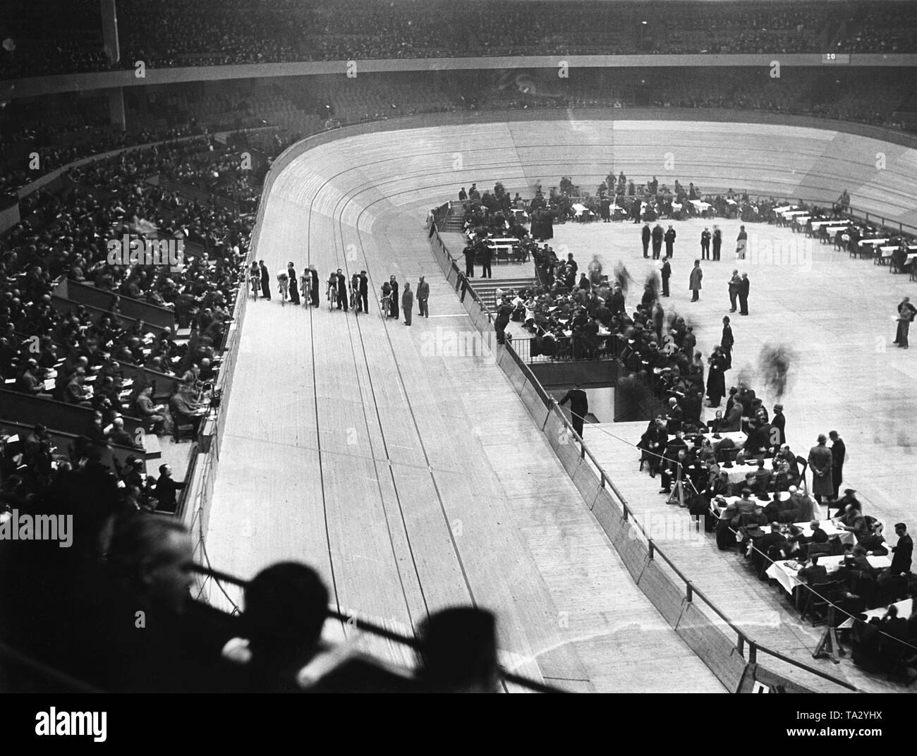 View of the cycling track and the spectator stands in the Berlin Deutschlandhalle, at an omnium race. On the track some road cyclists and their helpers stand ready for the start of a point race. Stock Photo