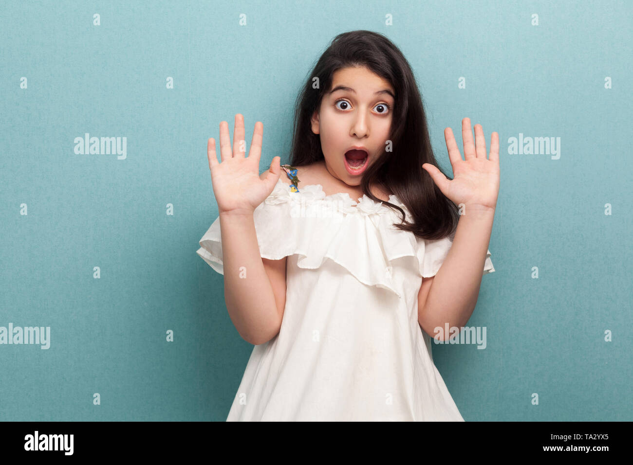 Portrait of shocked or scared beautiful brunette young girl with black long straight hair in white dress standing with hand block and looking at camer Stock Photo