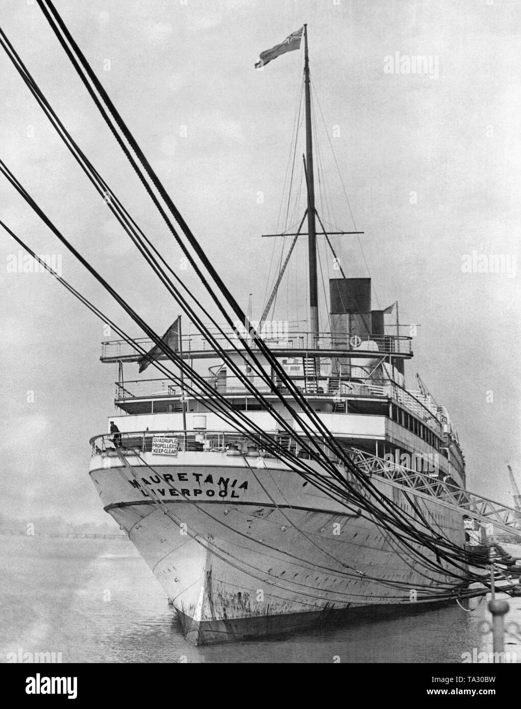 The 'Mauretania' with British naval flag for the throne jubilee of King George V in Southampton. The shield at the stern of the ship warns against the four propellers of the ocean liner. Stock Photo