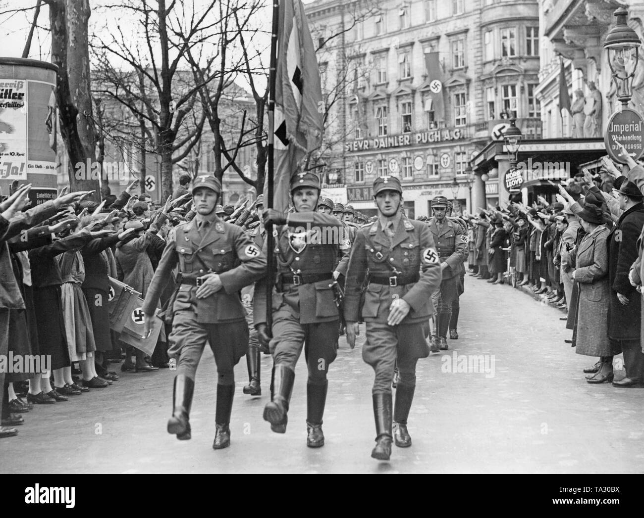 After the annexation of Austria to the German Reich, the Austrian legions return to Austria. The SA men march in front of the Vienna Hotel Imperial. In the background the lettering: 'Steyr Daimler Puch A.G.'. Stock Photo