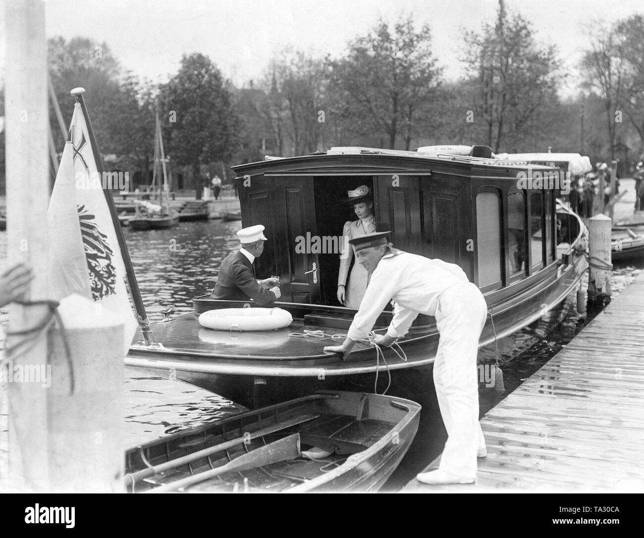 Crown Prince Wilhelm of Prussia (left sitting) with his wife Crown Princess Cecilie of Mecklenburg on a boat on the Havel. A sailor stands on the dock where the ship is secured and is unmooring. Stock Photo