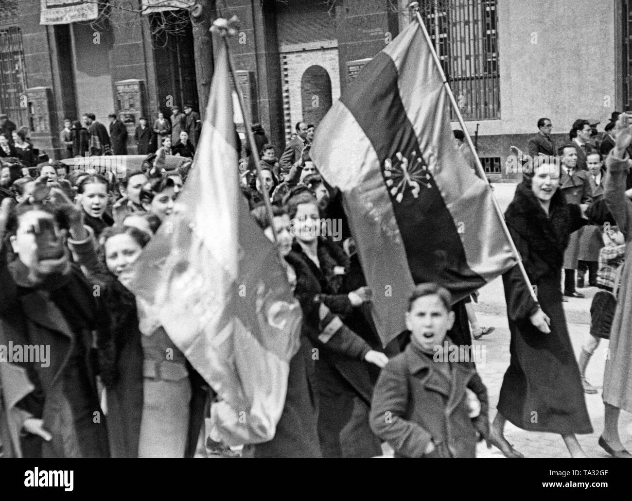 Supporters of General Franco walk through the streets of Madrid at the end of March after the entry of Franco's troops on March 28, 1939. The women raise the right arm in Fascist salute, on the red-blue flag at the front are the Yoke and Arrows as the symbol of the Fascist Party (Falange Espanola Tradicionalista de las JONS). Stock Photo
