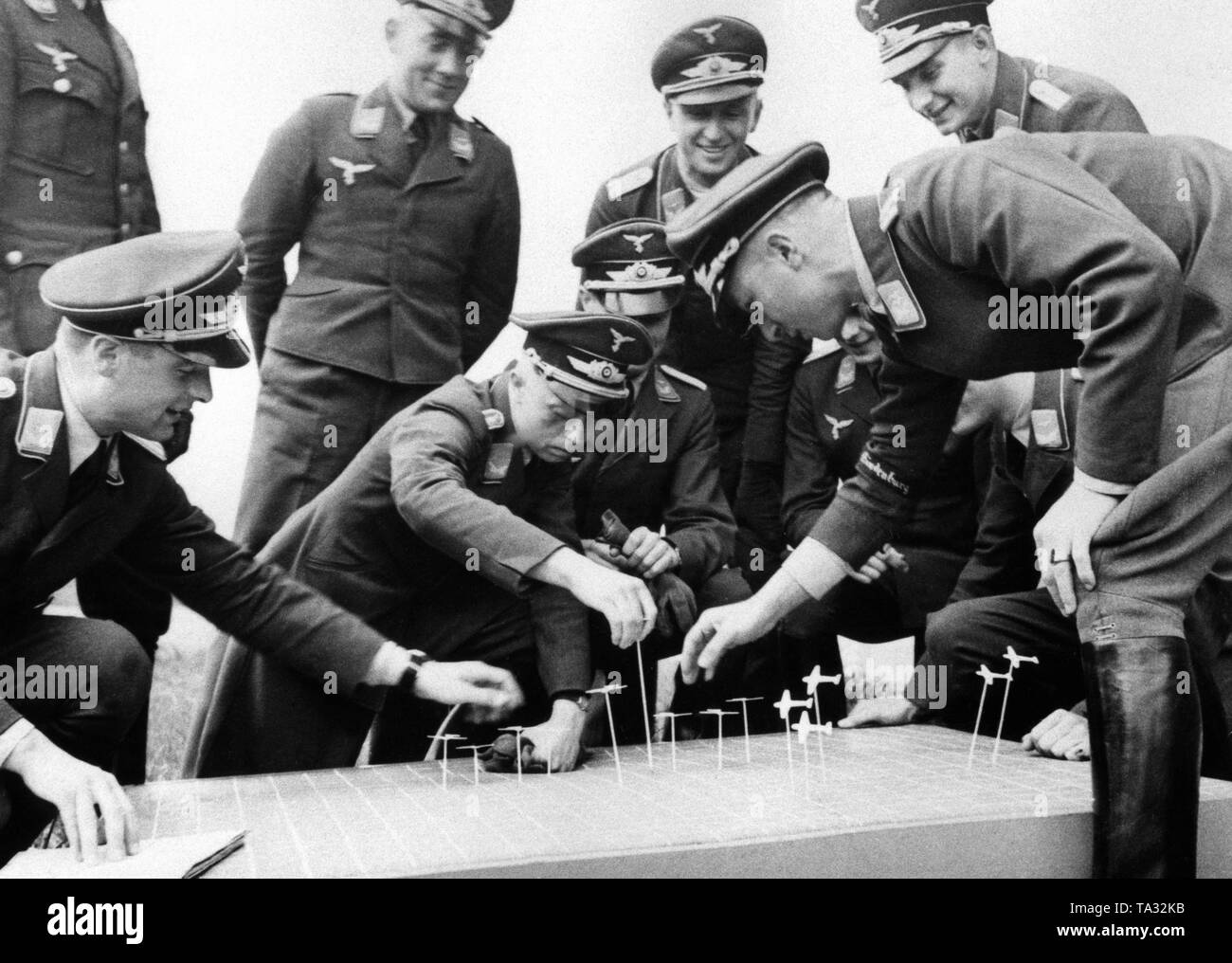 Officers of the Luftwaffe, of which the soldier in front right belongs to the Kampfgeschwader 1 'Hindenburg' bomber wing, practice tactical procedures on a model with small aircrafts. Stock Photo