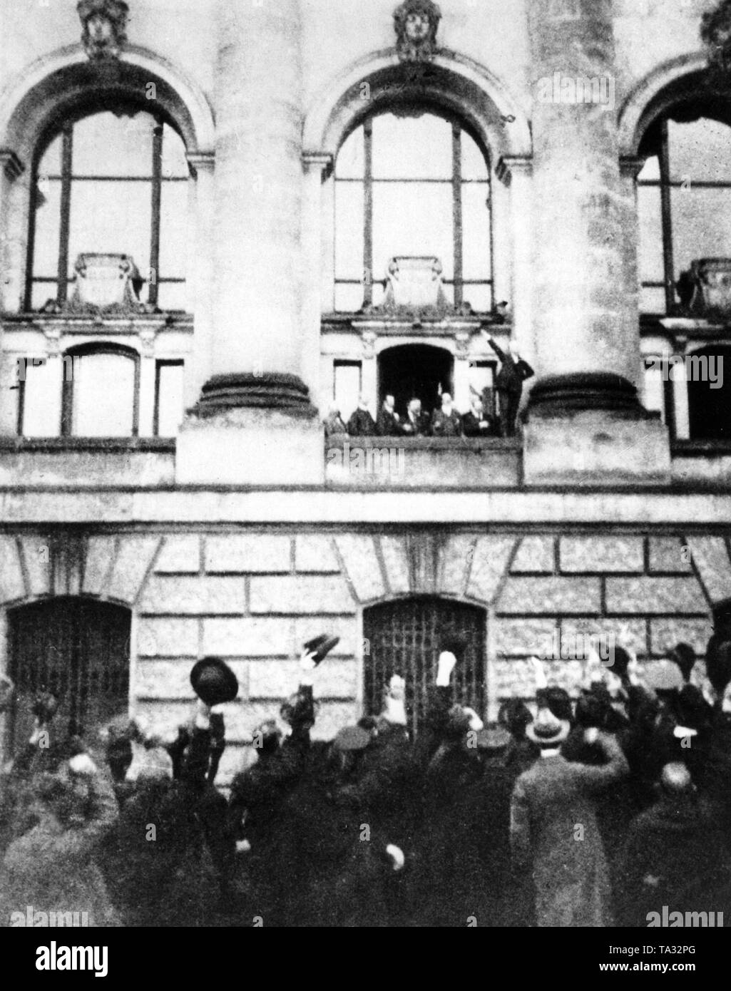 On 9 November 1918 Philipp Scheidemann (right on the balcony with an outstretched arm) proclaims the republic from a balcony of the Reichstag building. In the foreground people are waving. Stock Photo