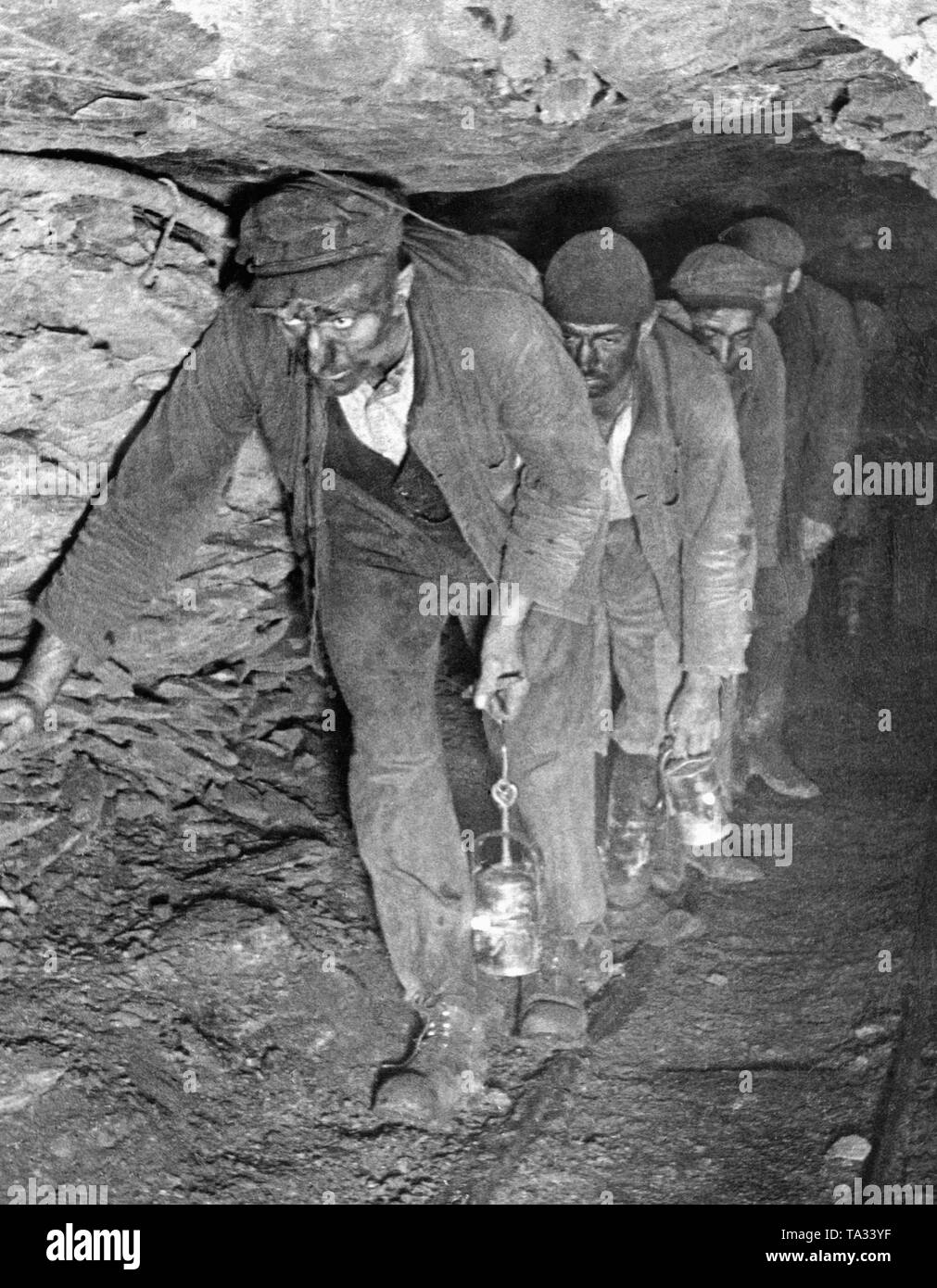Miners in a low tunnel in Saarland on the way back from work. Their faces are blackened by coal dust. They carry mine lights. Stock Photo