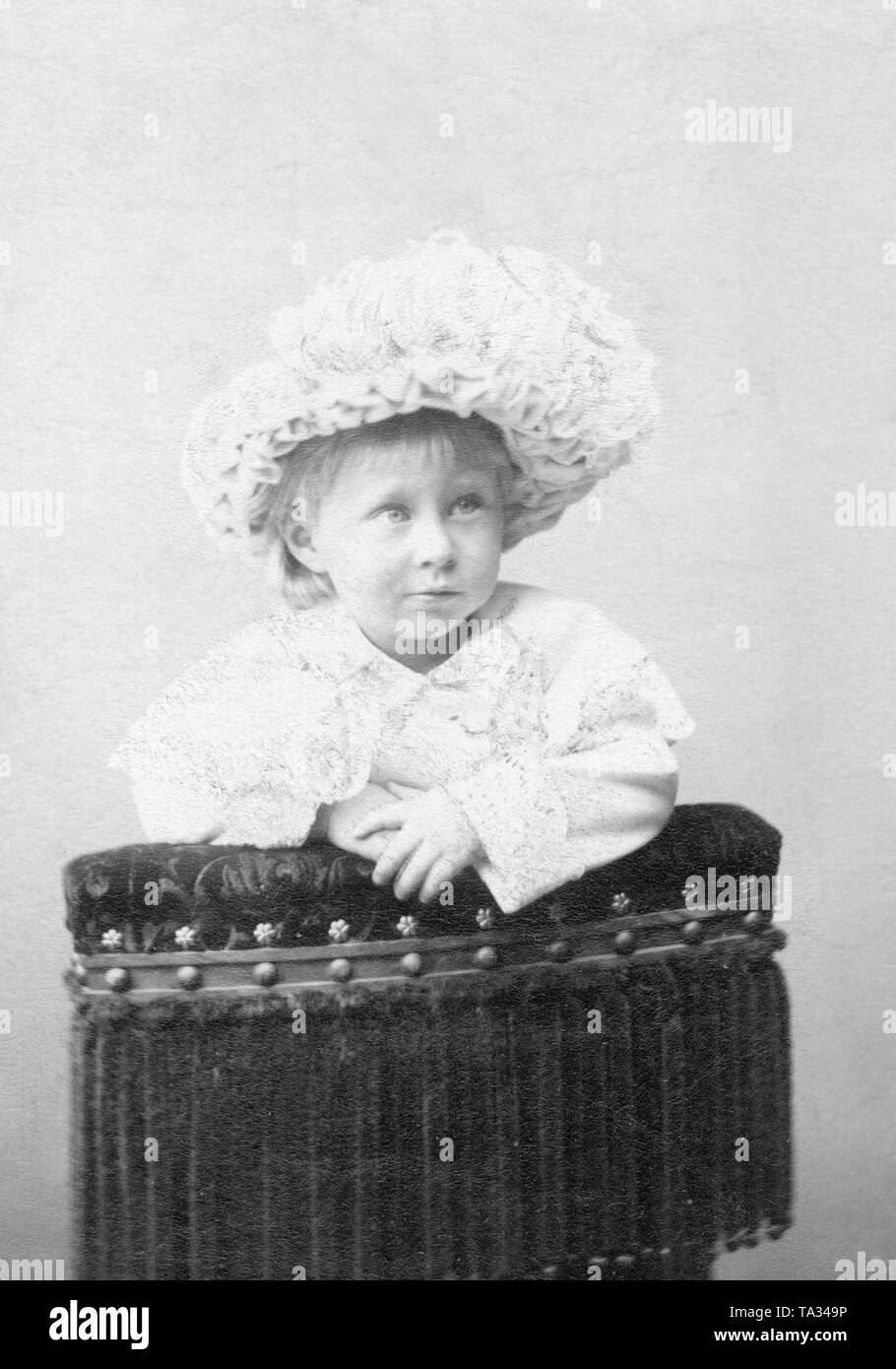 The picture shows the crown prince as a toddler in a white dress on a chair. Stock Photo