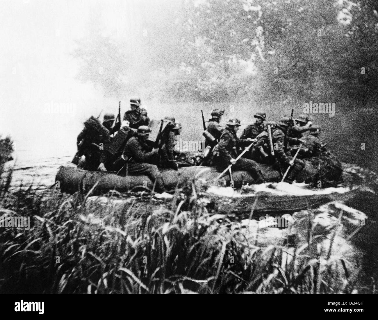 German signal troop (recognizable by the radio equipment of the men in center left) put a dinghy over a river. Probably a moviestill from Sieg im Westen (Victory in the West). Stock Photo