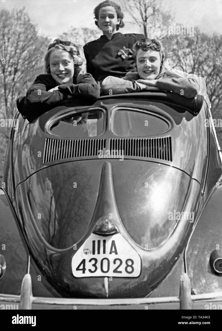 Three women in a VW Beetle. The first series are called 'Brezelkaefer' (Pretzel Beetles) because of their characteristic rear window. The number plate 'III A' stands for registration in Stuttgart. Stock Photo