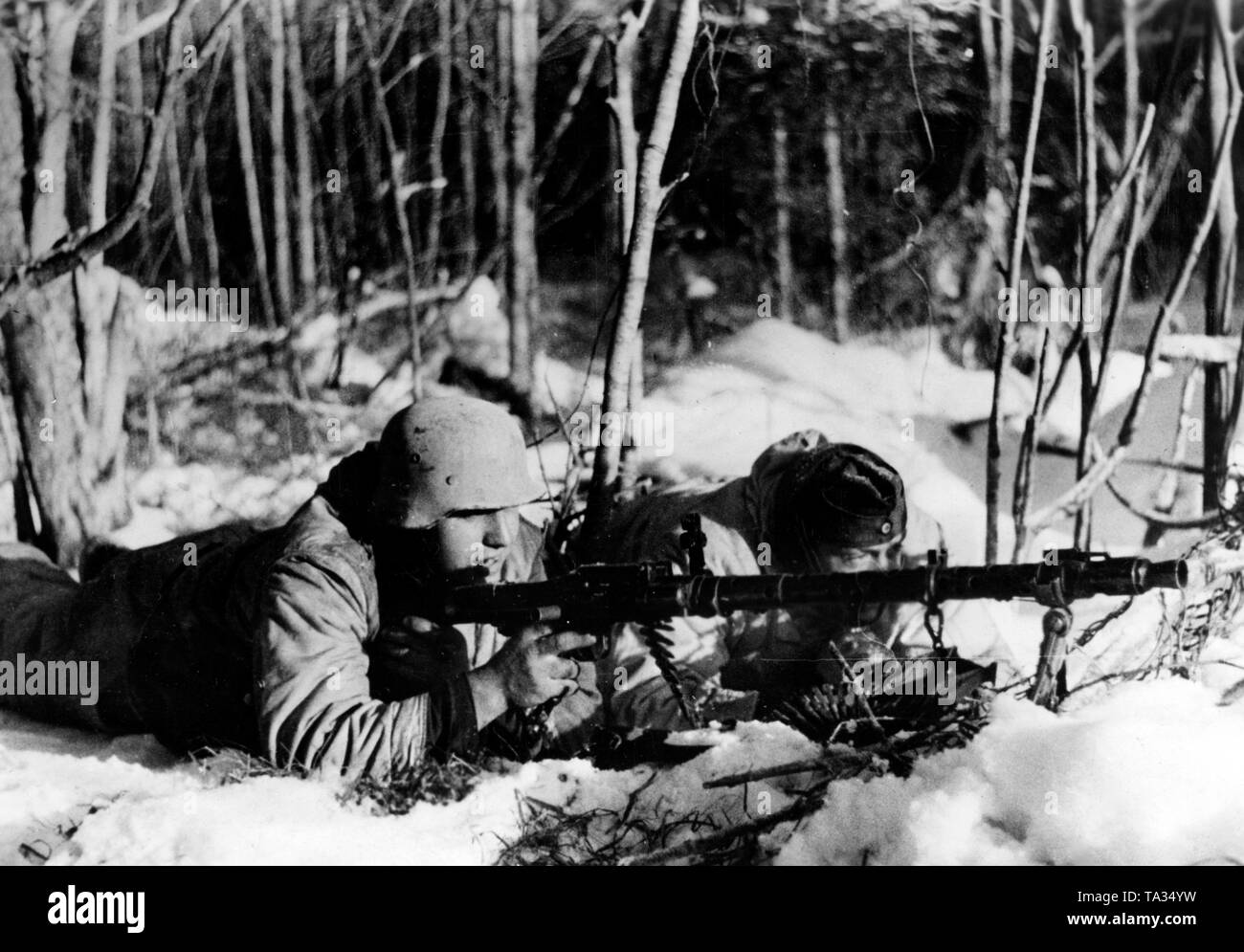 Two German soldiers lie in the snow in a forest on the Eastern Front. They are armed with a Maschinengewehr 34. Photo of the Propaganda Company (PK): war correspondent Maltry. Stock Photo
