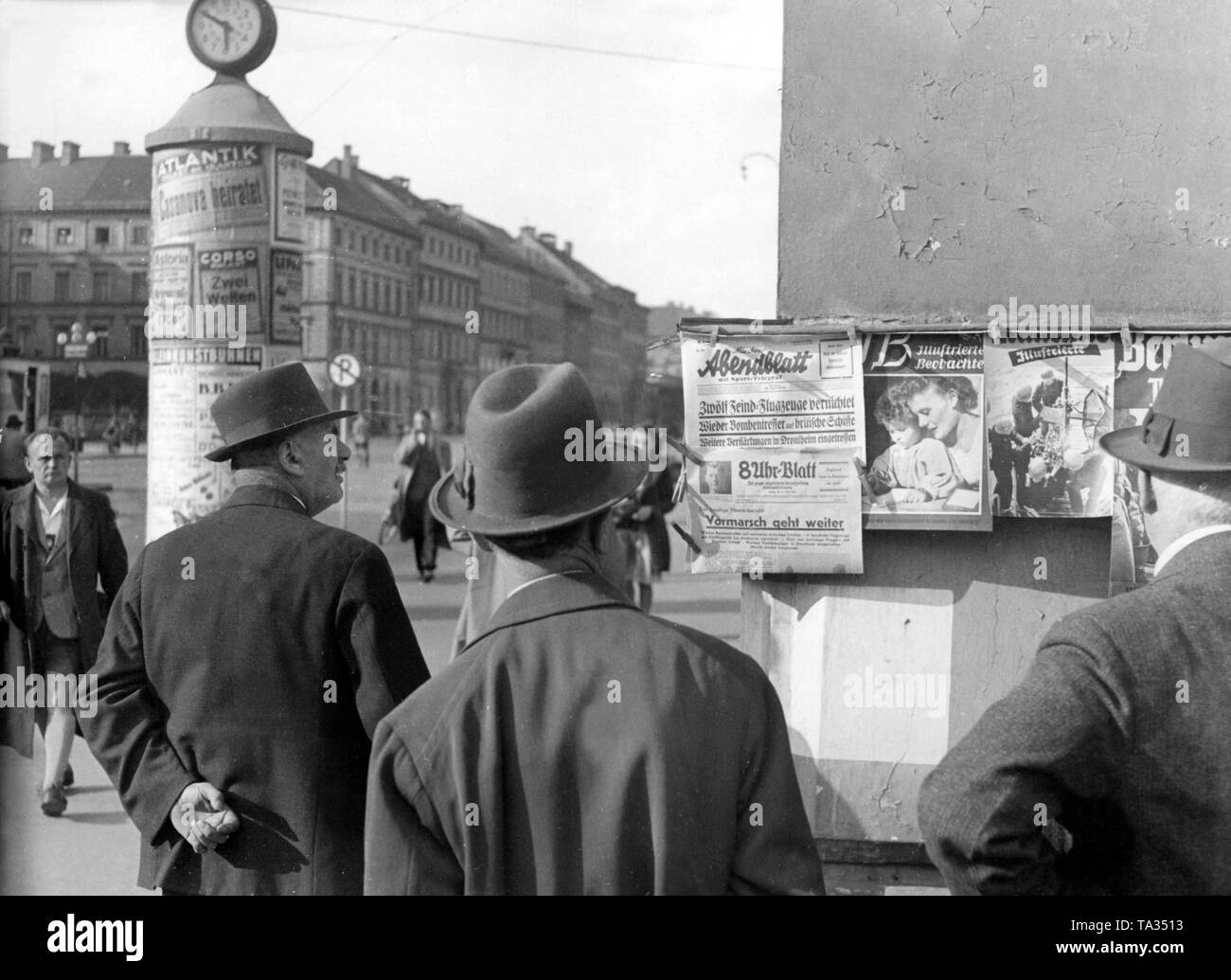 Passers-by observe newspaper displays at Odeonsplatz in Munich. On the front page of the  Münchner Abendblatts is reported: 'The advance continues'. The 'Illustrierte Beobachter' staged on its front page a harmonious family scene with mother and child. Stock Photo