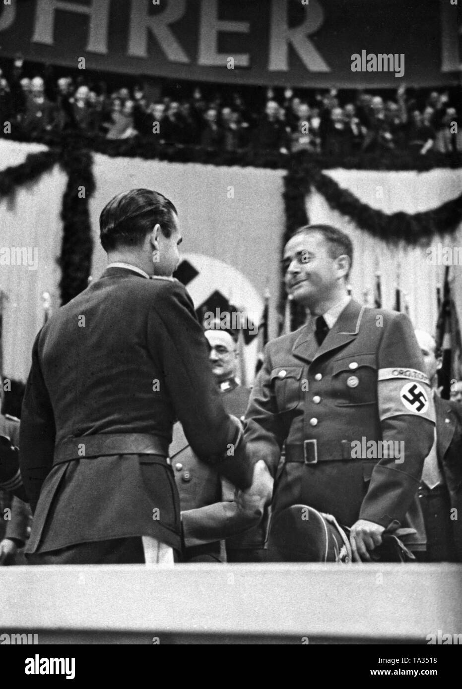 Adolf Galland (left) and Albert Speer shake hands at a mass rally in the Berlin Sportpalast. In the background, part of a banner with the inscription 'Fuehrer befiehl-wir folgen!' ('The leader commands, we follow'). Stock Photo