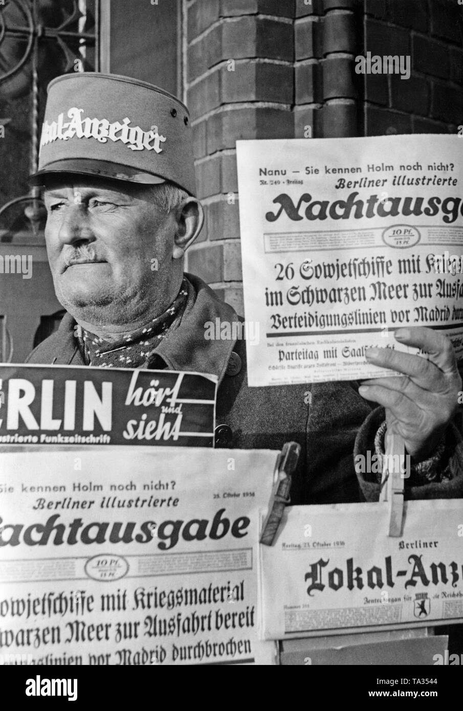 Photo of a newspaperman in Berlin, who sells a night edition of the Berliner Illustrierte of October 21, 1936. The newspaper headlines: '26 Soviet ships with war material ready for exit in the Black Sea', 'the defense line in front of Madrid collapsed'. Stock Photo