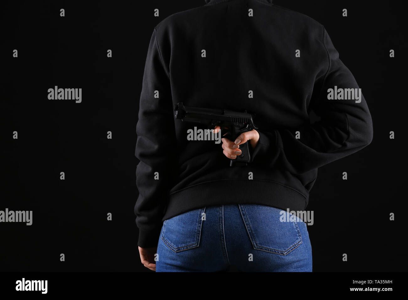 Person hiding gun behind back on dark background Stock Photo Alamy