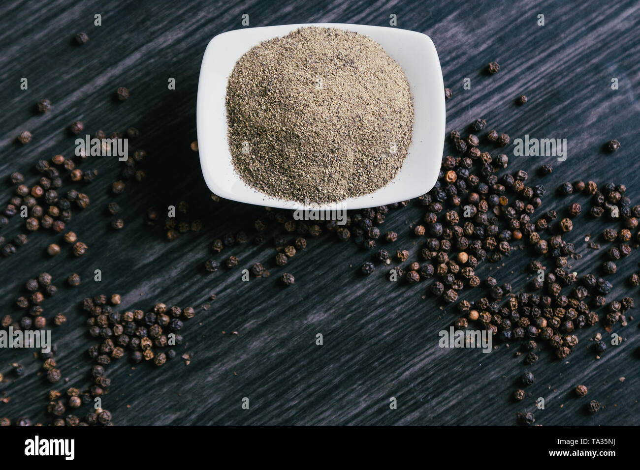 Black ground peppercorns in white bowl on wooden background. Stock Photo