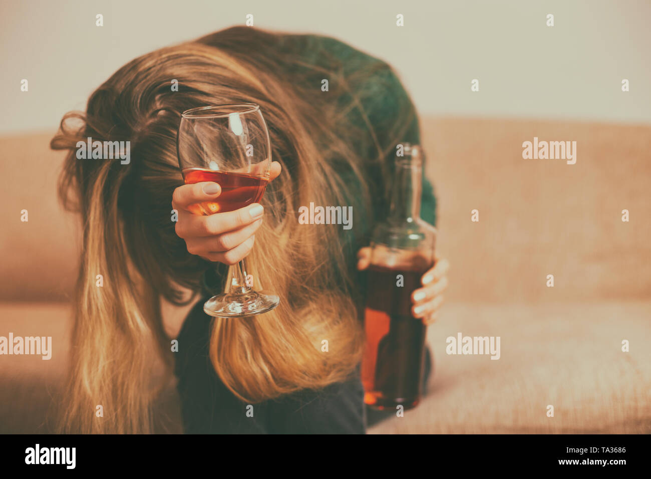 Depressed woman drinking alcohol while sitting alone at sofa.Toned image. Stock Photo
