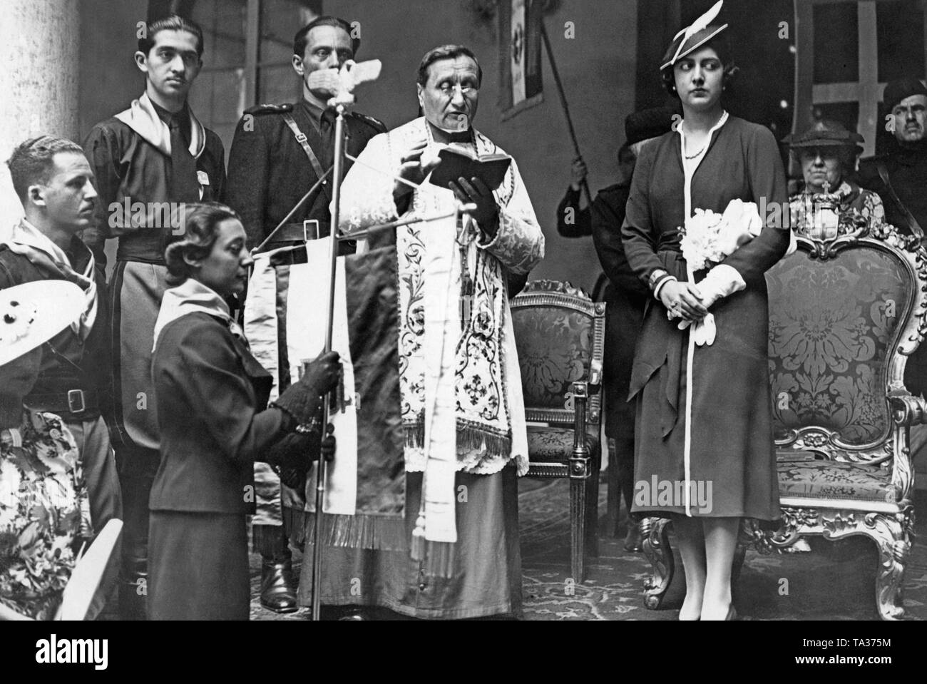 Mafalda, also Mary of Savoy, assists a priest in the blessing of a unit. The pennant 'Dante Alighieri' is handed over by a clergyman. After the conclusion of the Lateran Treaty in 1929, the relationship between the Italian state and the Vatican normalized. Stock Photo