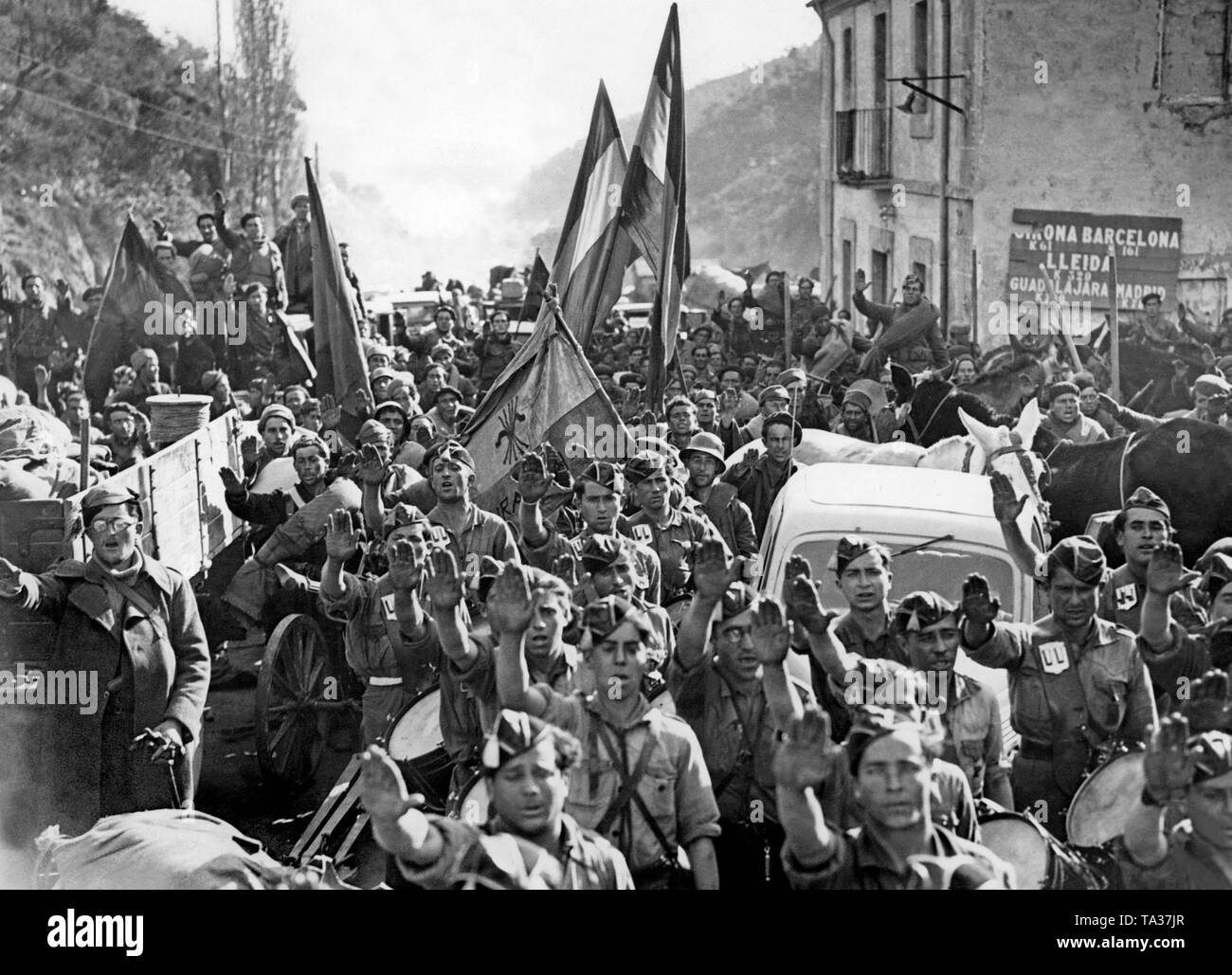 A unit of the Franco troops arrive on the Spanish-French border in Le Perthus on February 10, 1939. The soldiers greet with the Fascist salute. In the background is a flag of the Fascist Party (Falange Espanola Tradicionalista de las JONS). Stock Photo