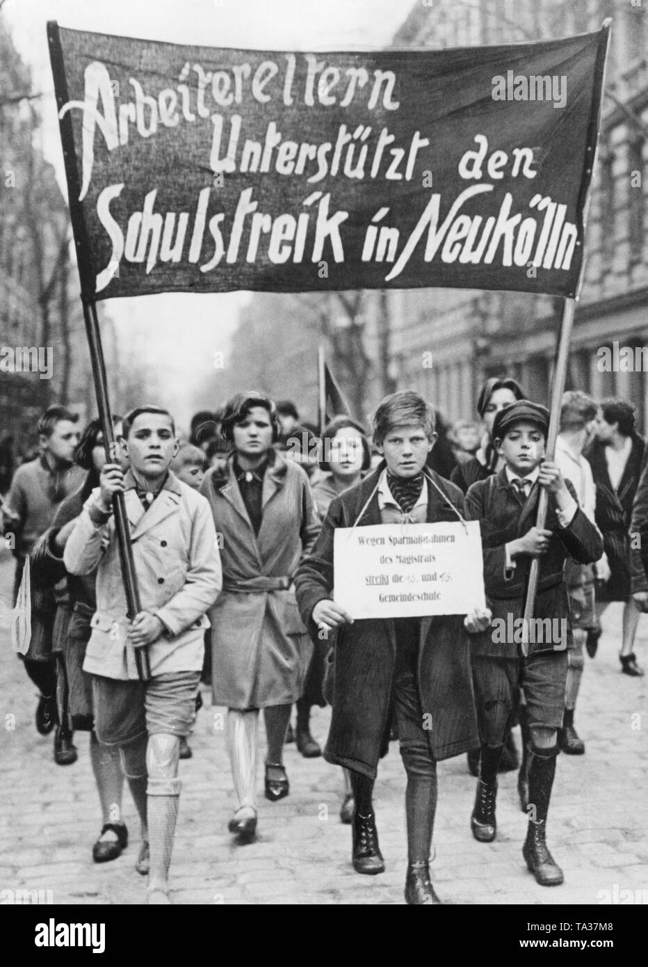 Striking students of the 15th and 16th Gemeindeschule (Municipal School) in Berlin-Neukoelln. They carry a banner with the slogan 'Worker parents support the school strike in Neukoelln'. A boy carries a sign around his neck saying 'Because of the austerity measures of the city council, the 15th and 16th Municipal School is on strike'. The background is the savings of the municipalities due to the global economic crisis. The KPD also used the strike to achieve its own party political goals. Stock Photo