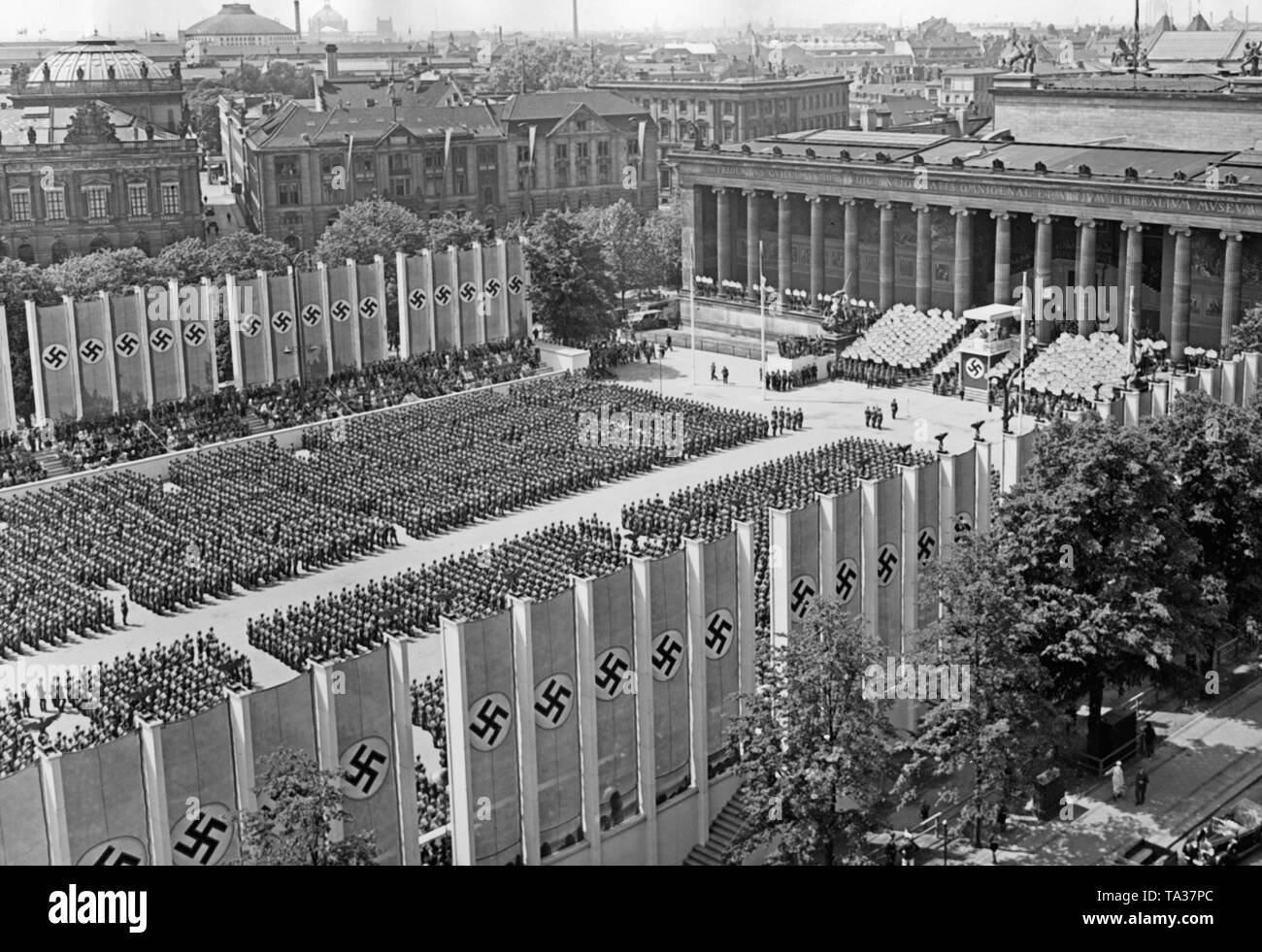 Photo of the fighters of the Condor Legion, who have stepped up in the Lustgarten after the parade. They are listening to the speech of Adolf Hitler (baldachin with swastika) in front of the Altes Museum in Mitte (Berlin) on the 6th of June, 1939. On the right and on the left there are grand stands. On the stairs next to the lectern, members of the Hitler Youth are standing with signs depicting the names of the fallen legionaries in Spain. Stock Photo