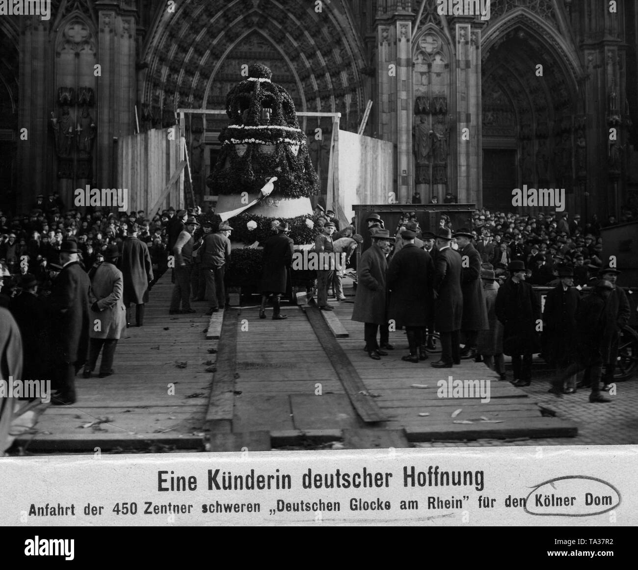 Arrival of the new bell for the Cologne Cathedral, the 'Deutsche Glock am Rhein', on 14.11.1924. The bell is decorated with flowers. At the bell, the workers who brought it to the South Tower. Left and right, the ramp with which it was transported to the Cathedral, spectators.In the background, the portals of the Cathedral. Stock Photo