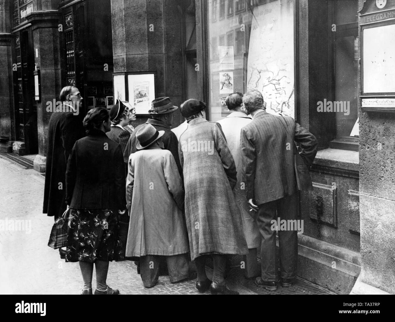 A group of passers-by in front of a notice board at the building of the publisher Knorr & Hirth (Munchner Neueste Nachrichten) in Sendlinger Strasse, Munich. On the map the British Isles, so it's probably about the Battle of Britain 1940/41. Undated photo. Stock Photo