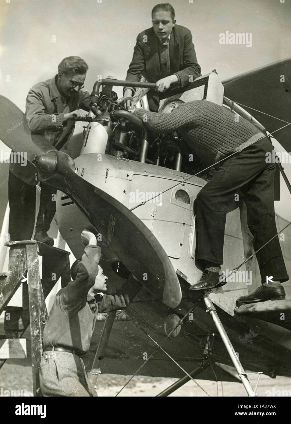 Young unemployed people repairing an aircraft engine of a pre-war biplane, which is used to launch gliders. Trainings, as here, for aircraft mechanics, often served as a job creation scheme. Stock Photo