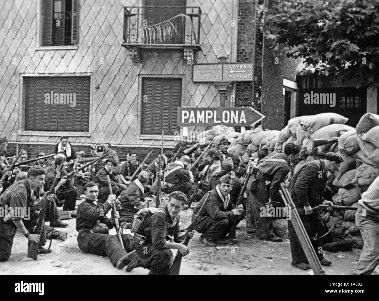Photo of a unit of Republican fighters in blue overalls, presumably volunteers of the anarcho-syndicalist FAI / CNT. The fighters armed with guns have entrenched themselves  behind a sandbag barricade in the Spanish border town of Irun on the exit road towards Pamplona, ??Navarre. In the other direction, the French border. Stock Photo