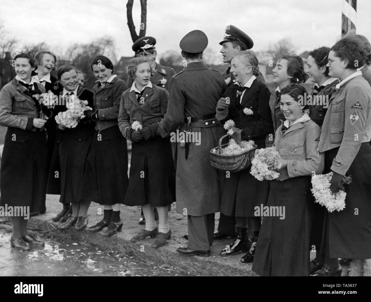Girls of the BDM greet soldiers of the Luftwaffe as they march with flowers. They build up a military airfield with fighter pilot school in Werneuchen that has become a garrison. Stock Photo