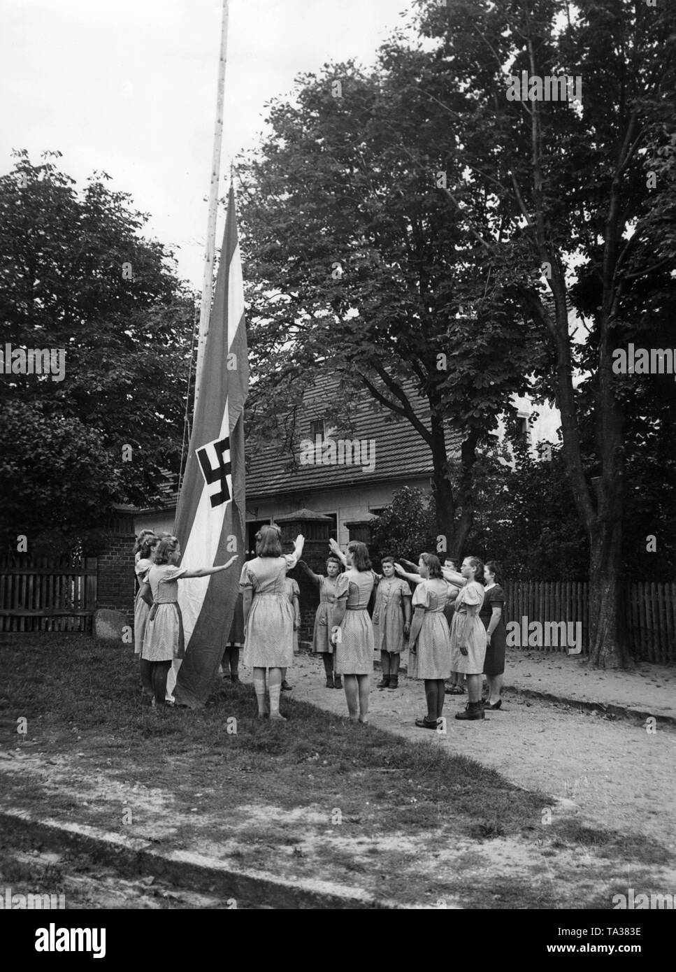 BDM girls perform the Nazi salute in front of a swastika flag at the morning assembly in the agricultural camp. As a military service they do agricultural work in the Warthegau area. Stock Photo