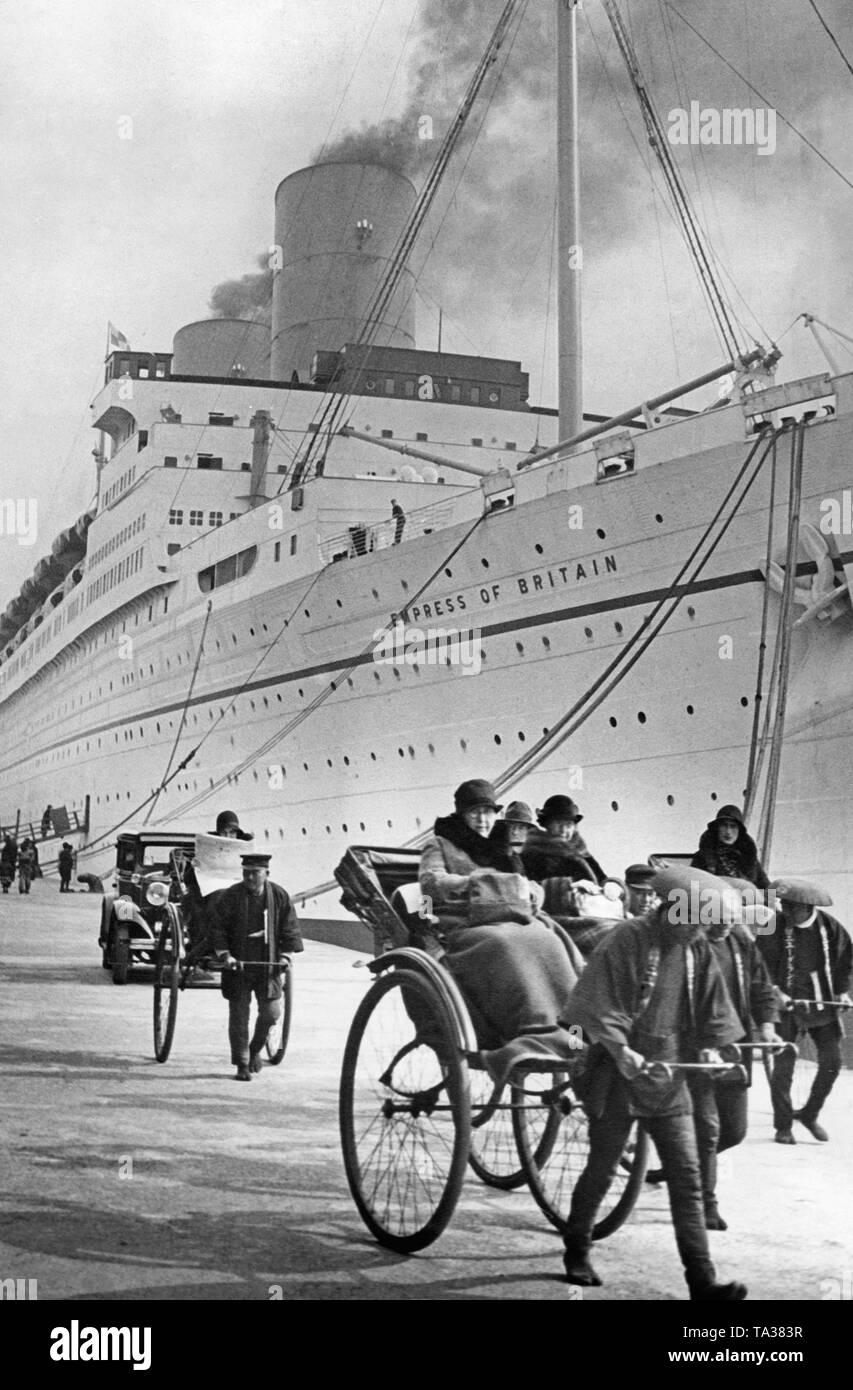 A group of Europeans ride in rickshaws through the port of Tokyo. In the background the ship 'Empress of Britain'. Stock Photo