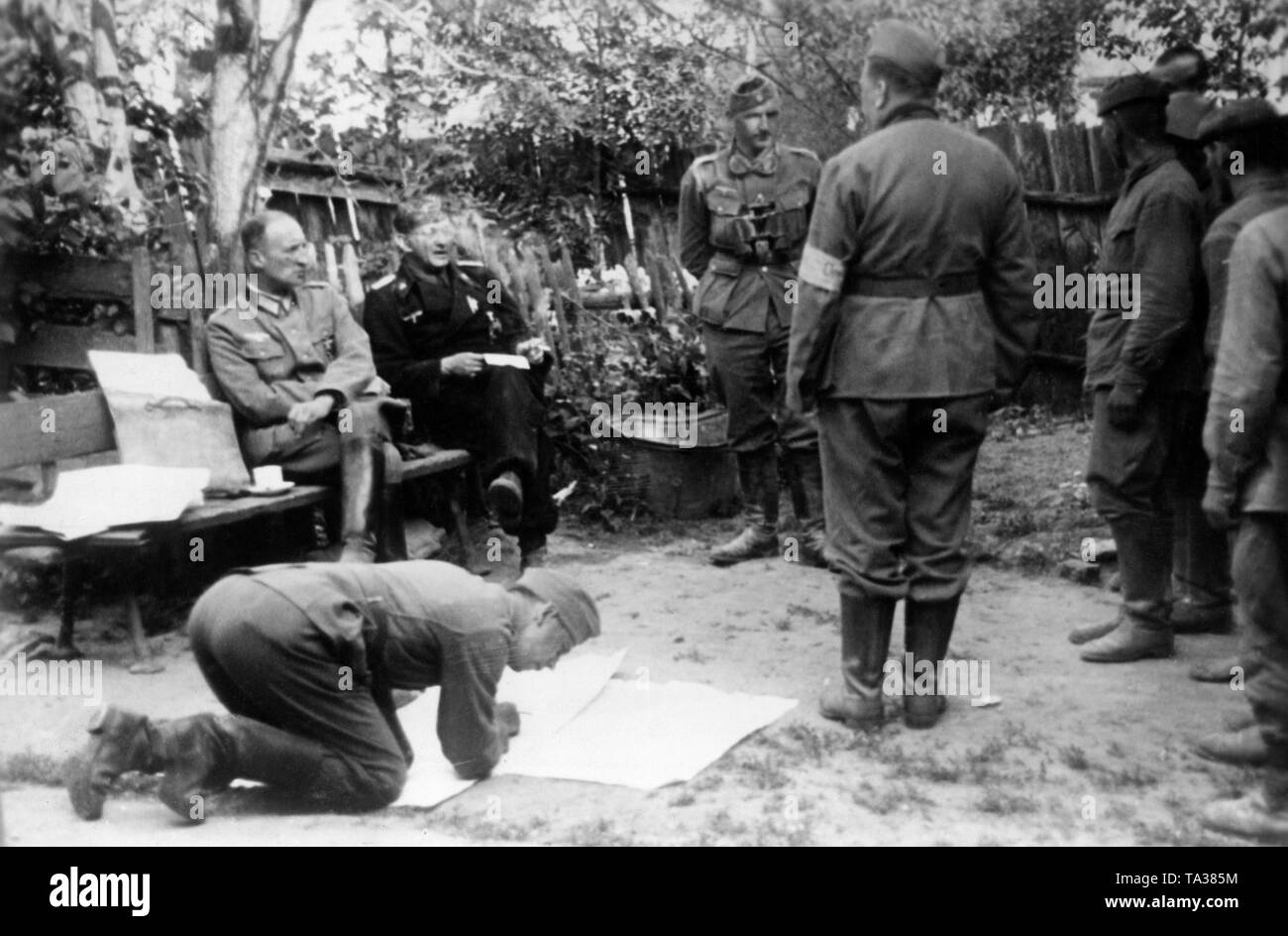 Russian prisoners are interrogated by officers of the Wehrmacht on the eastern front near Panjewitsch. Sitting on the bench, a staff officer and an officer of the Panzertruppe, on the left soldiers of the Red Army. Photo: war reporter Tannenberg. Stock Photo