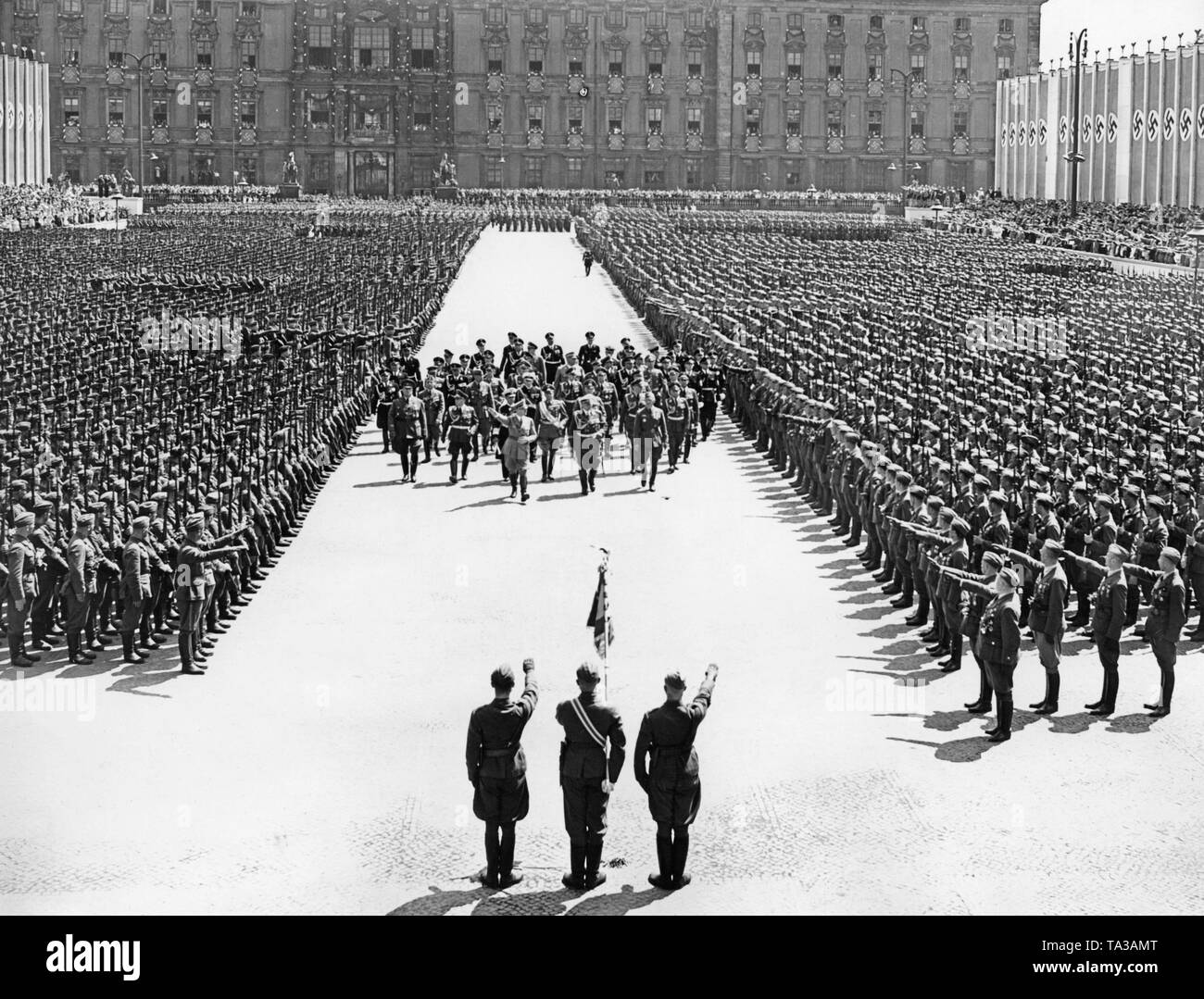 Adolf Hitler and Field Marshal General Hermann Goering (middle, the first row), along with other prominent figures (including Major General Wolfram von Riochthofen, Grand Admiral Erich Raeder, General Wilhelm Keitel, General der Flieger Hugo Sperrle, SS leader Heinrich Himmler), are marching through the Lustgarten in Berlin-Mitte among the lines of the Condor Legion (giving the Hitler salute) towards the lectern in front of the Altes Museum. They are received by color guards of the Legion. In the background, the facade of the Berlin Palace. Stock Photo