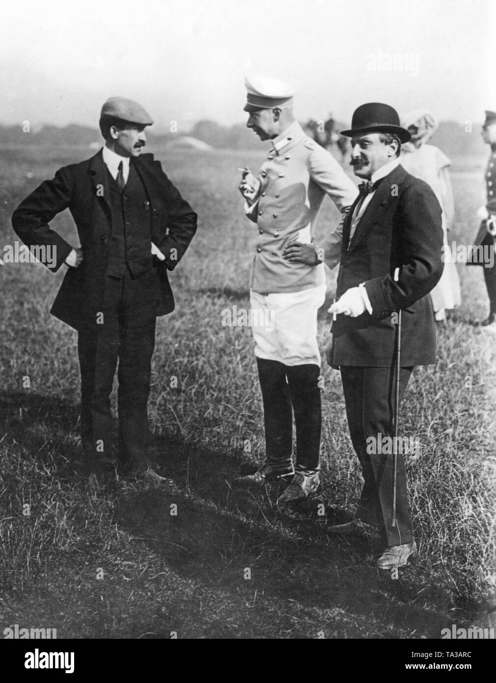 Crown Prince Wilhelm (middle) arrived, together with his wife Crown Princess Cecilie of Prussia born Duchess of Mecklenburg, (2nd from right), to the airfield Tempelhof Field to follow the flight demonstration of Orville Wright (left). Here, the Crown Prince having a conversation with the famous aviator. Stock Photo