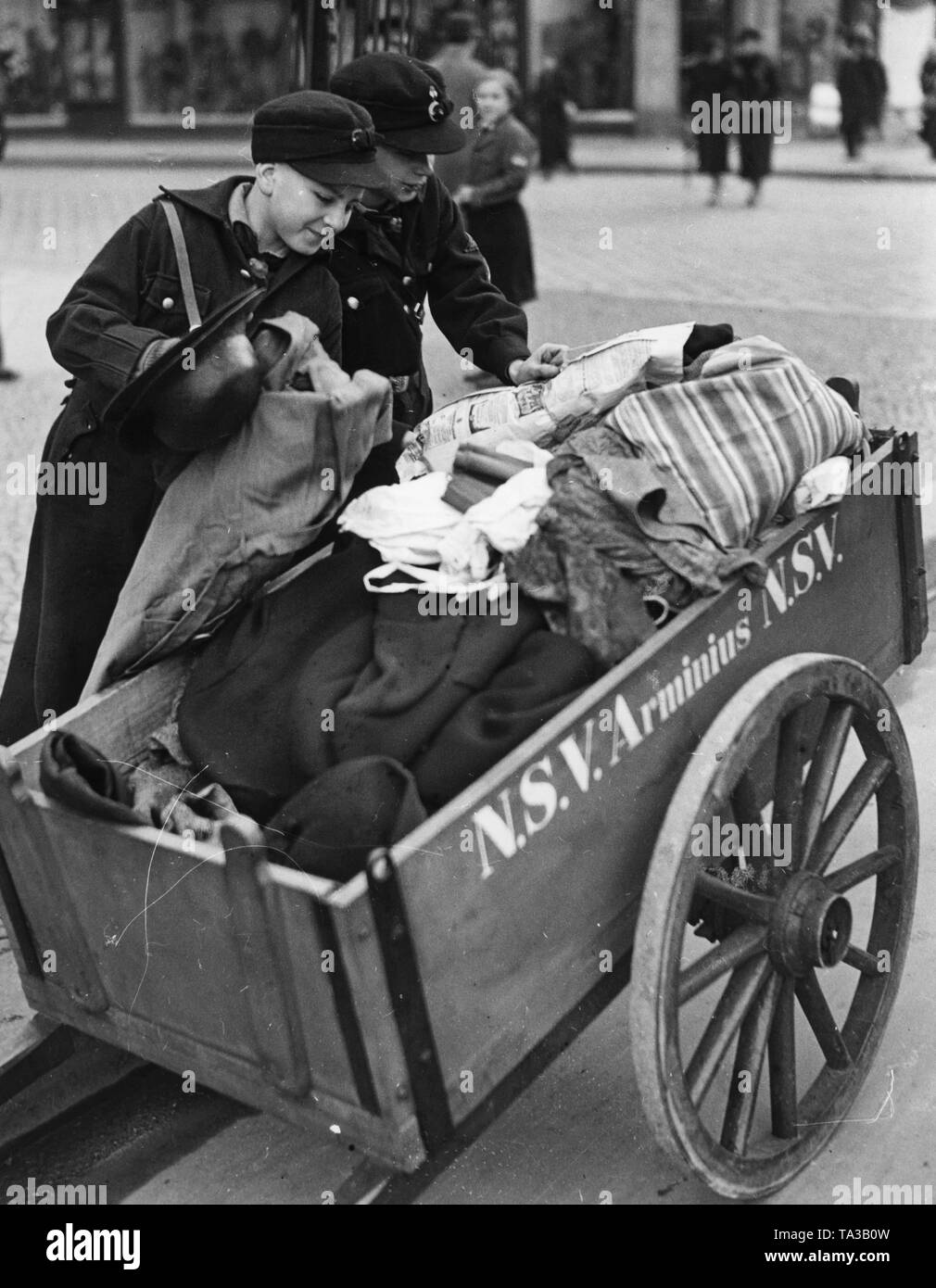 Pimpfs of the Hitlerjugend (Hitler Youth) are loading a pushcart of the NS-Volkswohlfahrt 'Arminius' with donation clothes for the Winterhilfswerk. Stock Photo