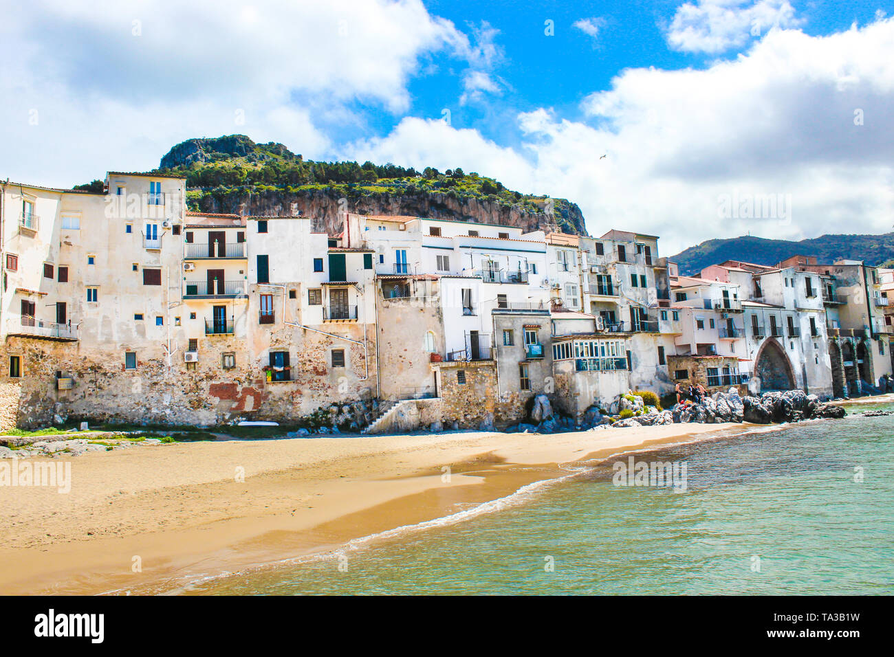 Traditional historical houses on the coast of Tyrrhenian sea in Sicilian Cefalu, Italy. Behind the houses there is rock overlooking the city. The beautiful Italian city is popular tourist attraction. Stock Photo