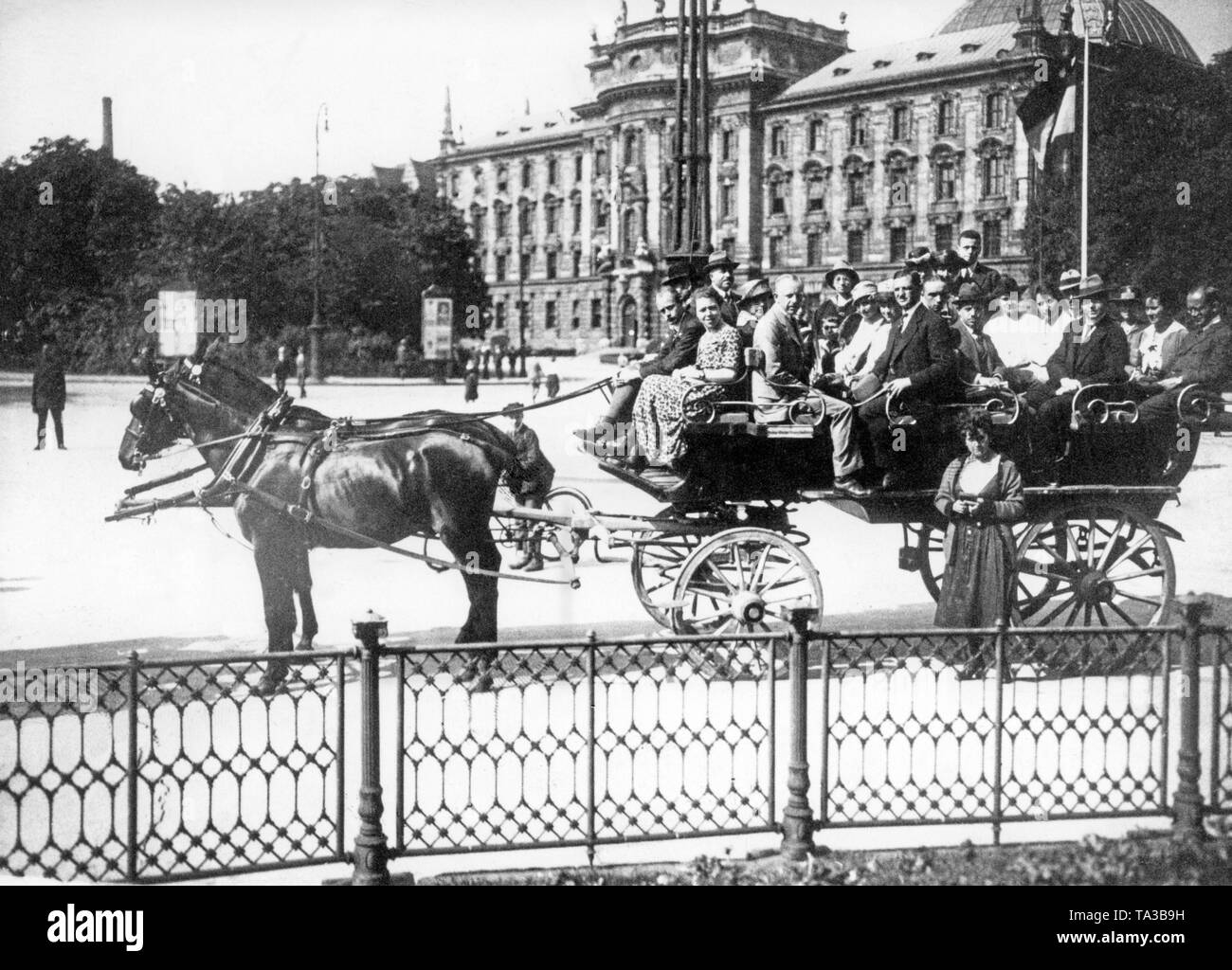 Tourists take a city tour with a horse-drawn carriage in Munich. In the background is the Palace of Justice on the edge of the Karlsplatz / Stachus. Stock Photo