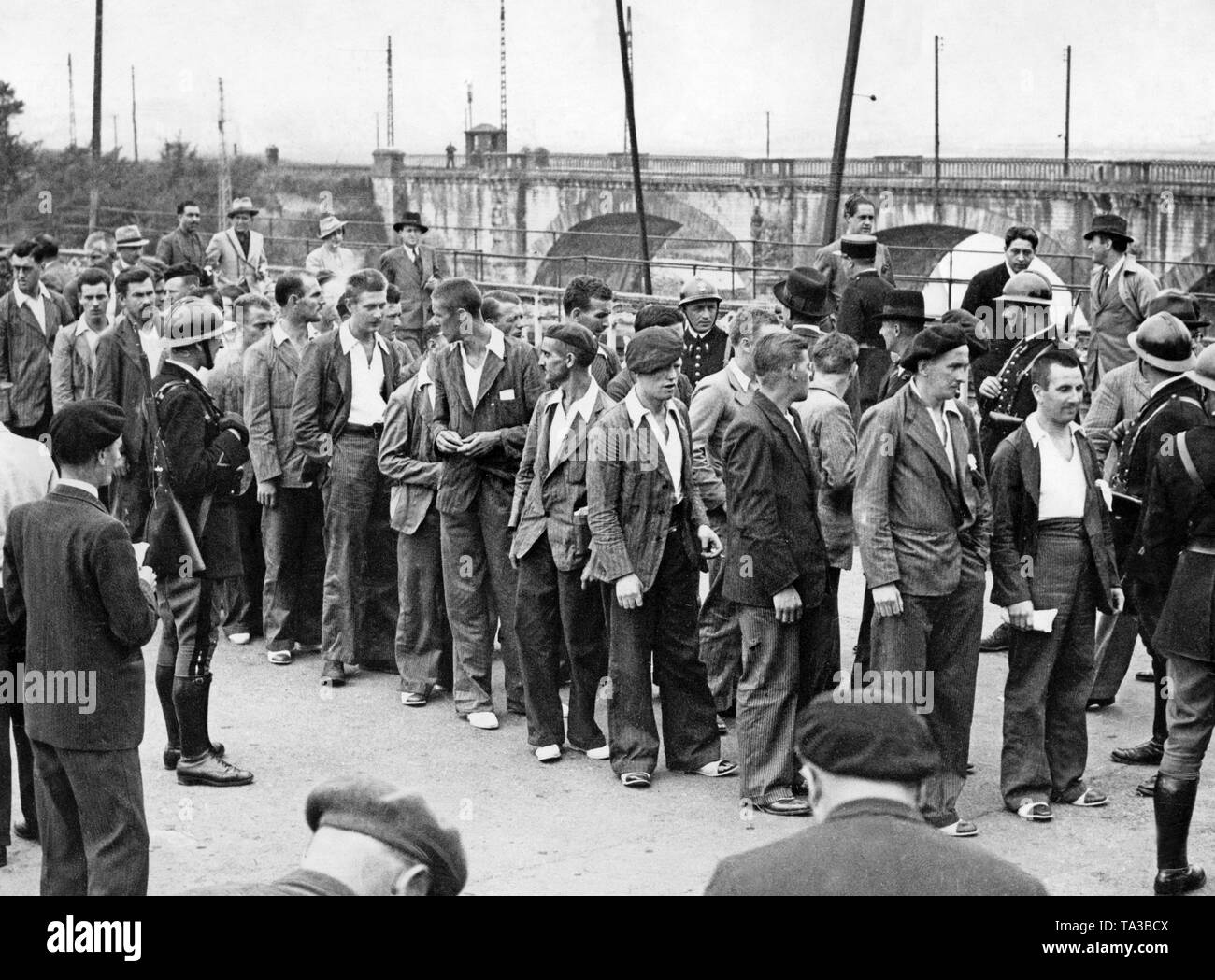 Photo of a group of 50 Spanish Republican militiamen after their crossing the border from Spain to France in Hendaye in the French Basque country. The men in civilian clothes, who were received by French gendarmes, a commission of the non-interference committee and journalists, had previously been released by the commander-in-chief of the Spanish national faction General Francisco Franco. In the background, the border bridge and a Spanish custom house. Stock Photo