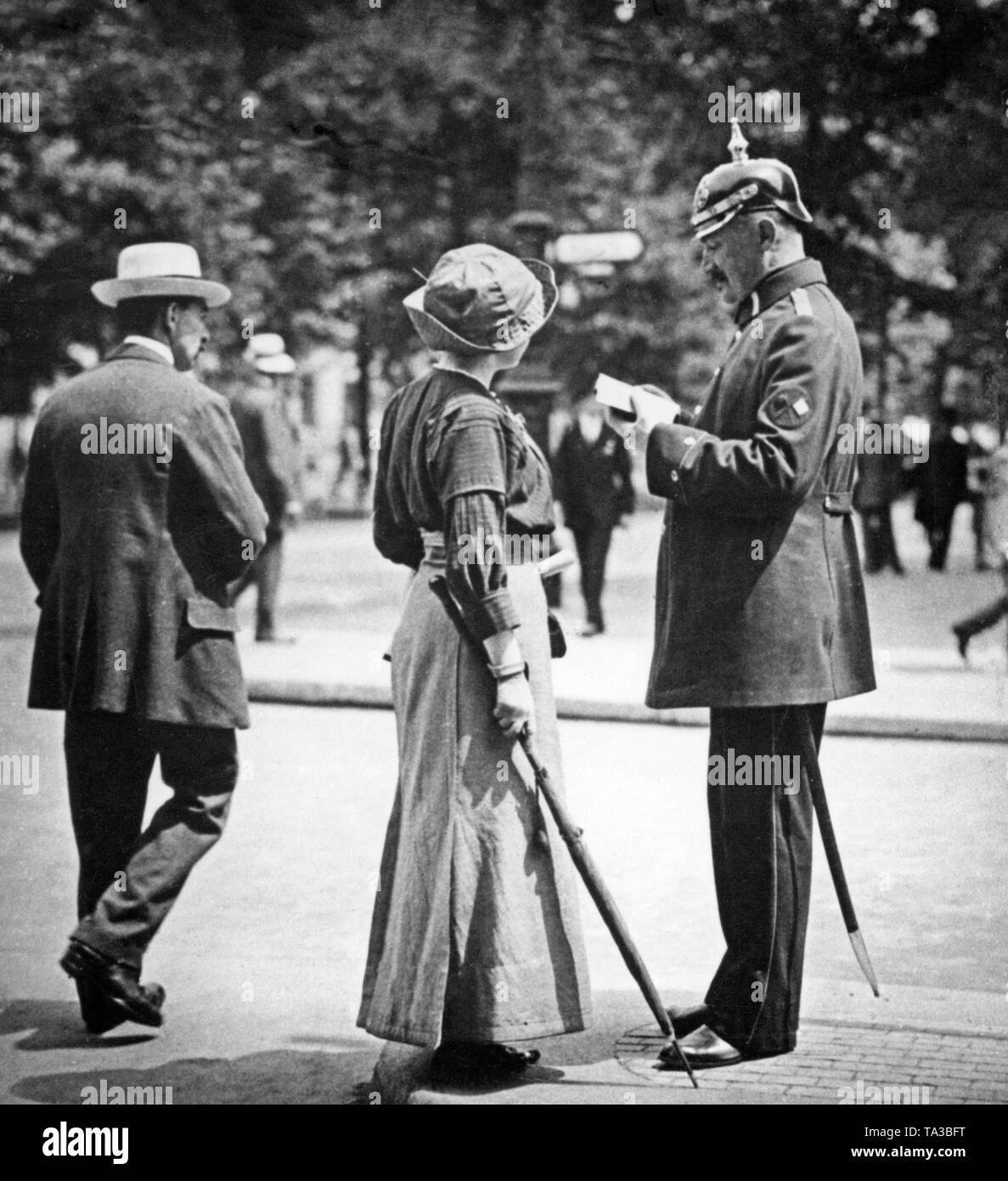 A tourist asks a policeman for directions. The policeman wears a spiked helmet and a saber. Stock Photo