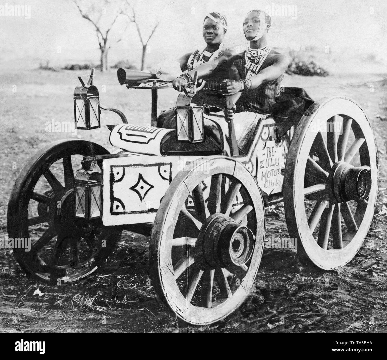 Two Zulu girls sit in a car made of coach wheels and boards Stock Photo