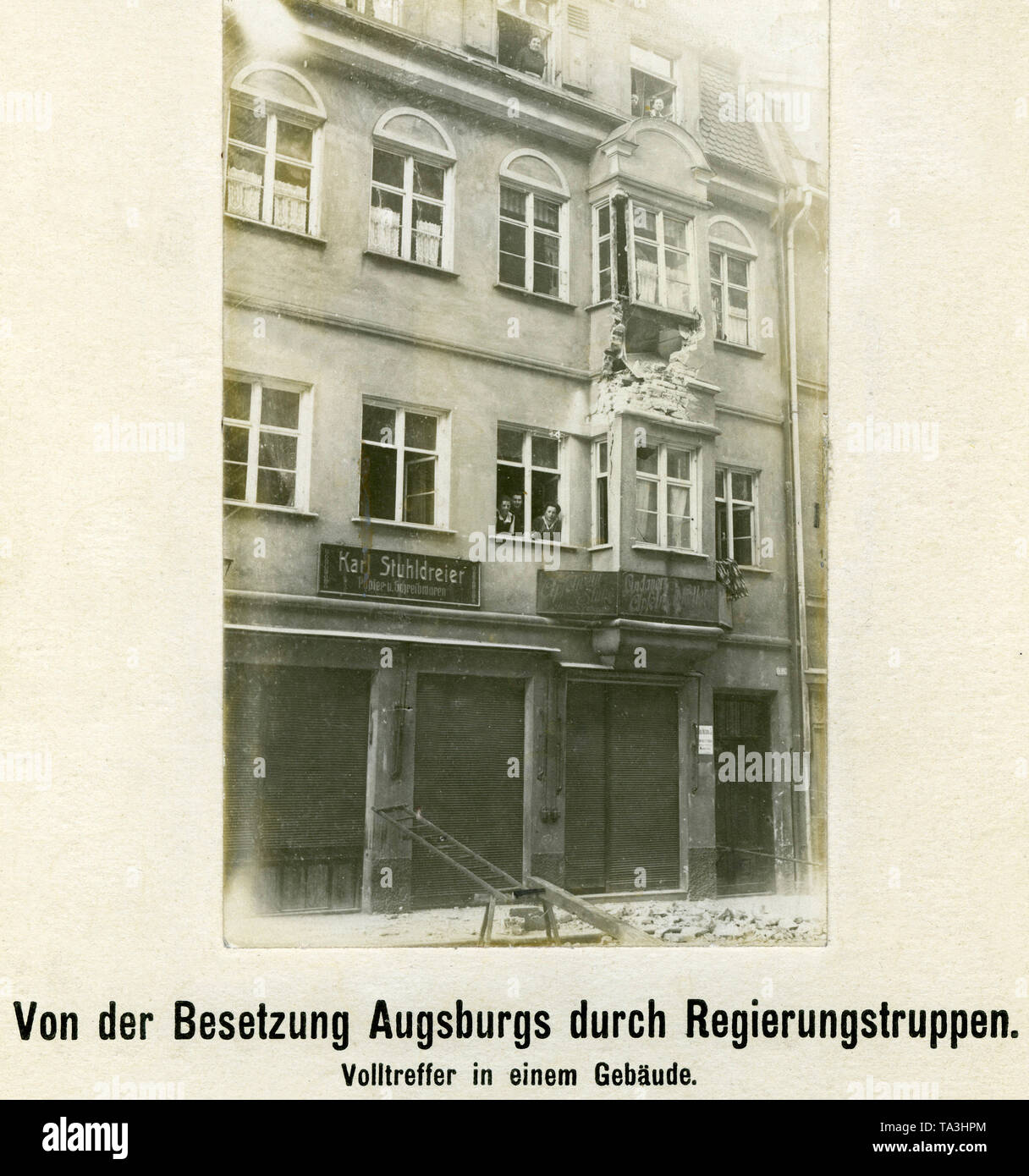 The picture shows a building damaged by a hit in Augsburg after the occupation by government troops on Easter 1919 (called 'bloody Easter' by the Augsburgs). Residents watch the photographer from their windows. Stock Photo