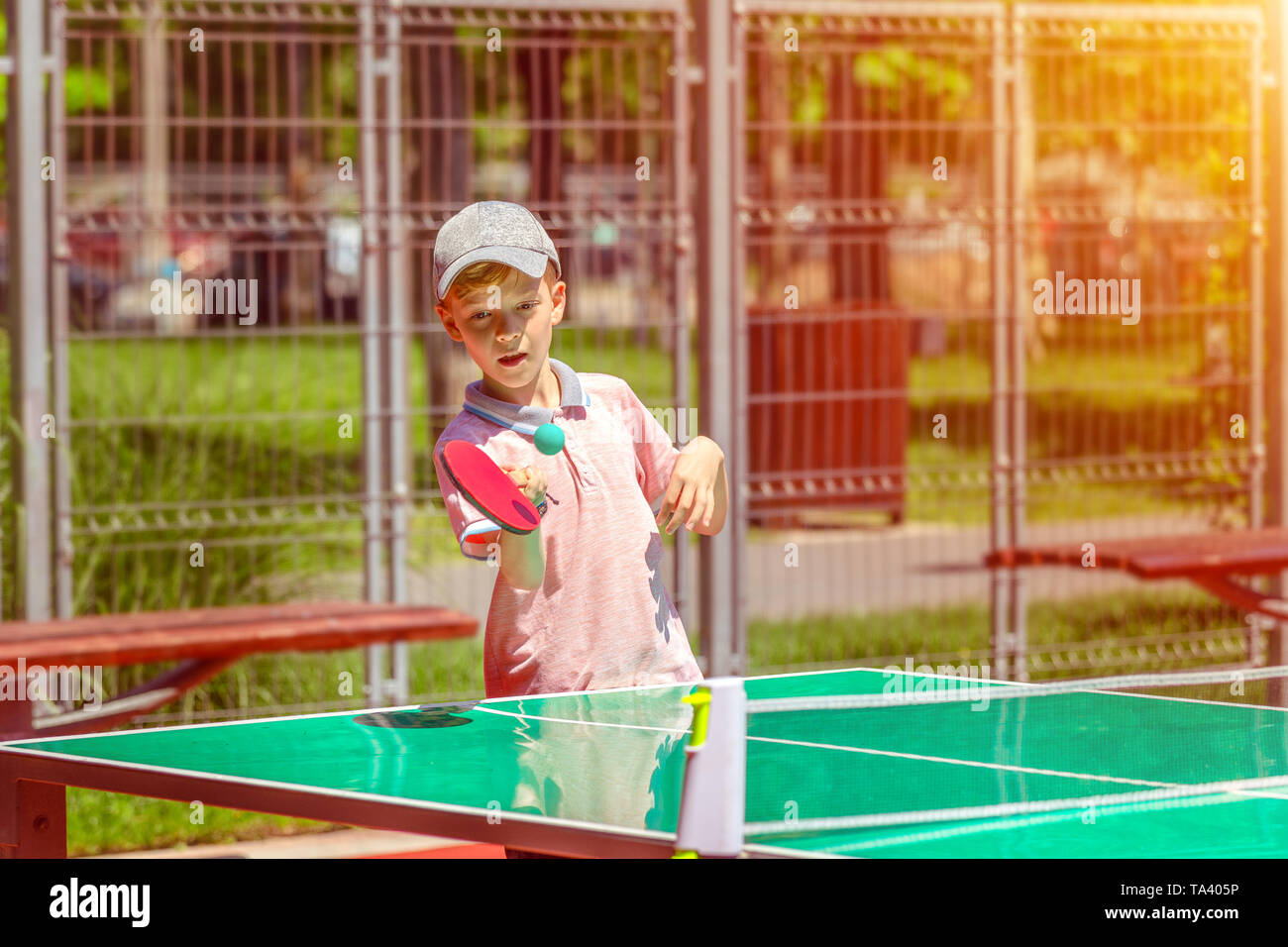 Cute little boy playing table tennis in park – outdoor activity in sport ground with smiling kid having fun learning and practicing ping pong Stock Photo