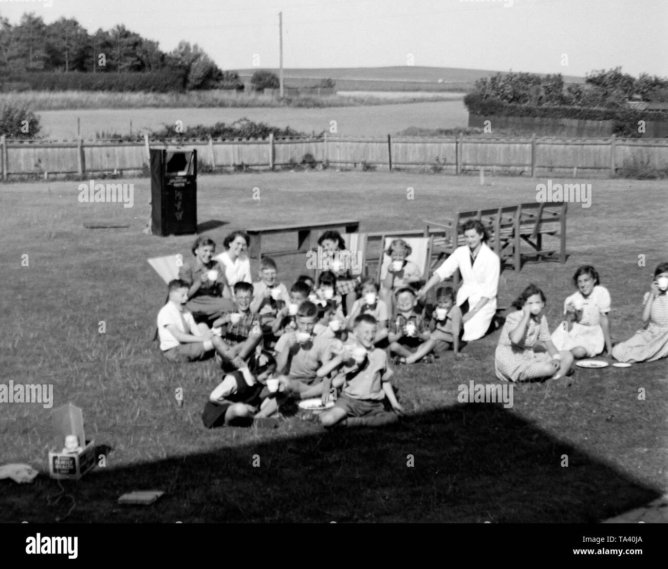 Children at Gracie Fields orphanage in Peacehaven, Sussex around 1956 having tea in the grounds in the background a Punch & Judy show is being set up Stock Photo
