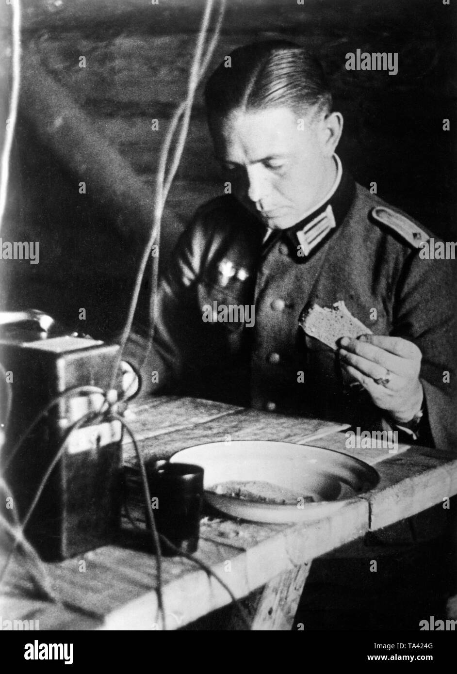 A lieutenant in the army, duty officer at work during the Battle of Moscow. He is eating a slice of bread between phone calls with the front and drawing of reconnaissance results. Photo: war correspondent Sepp Jaeger Stock Photo