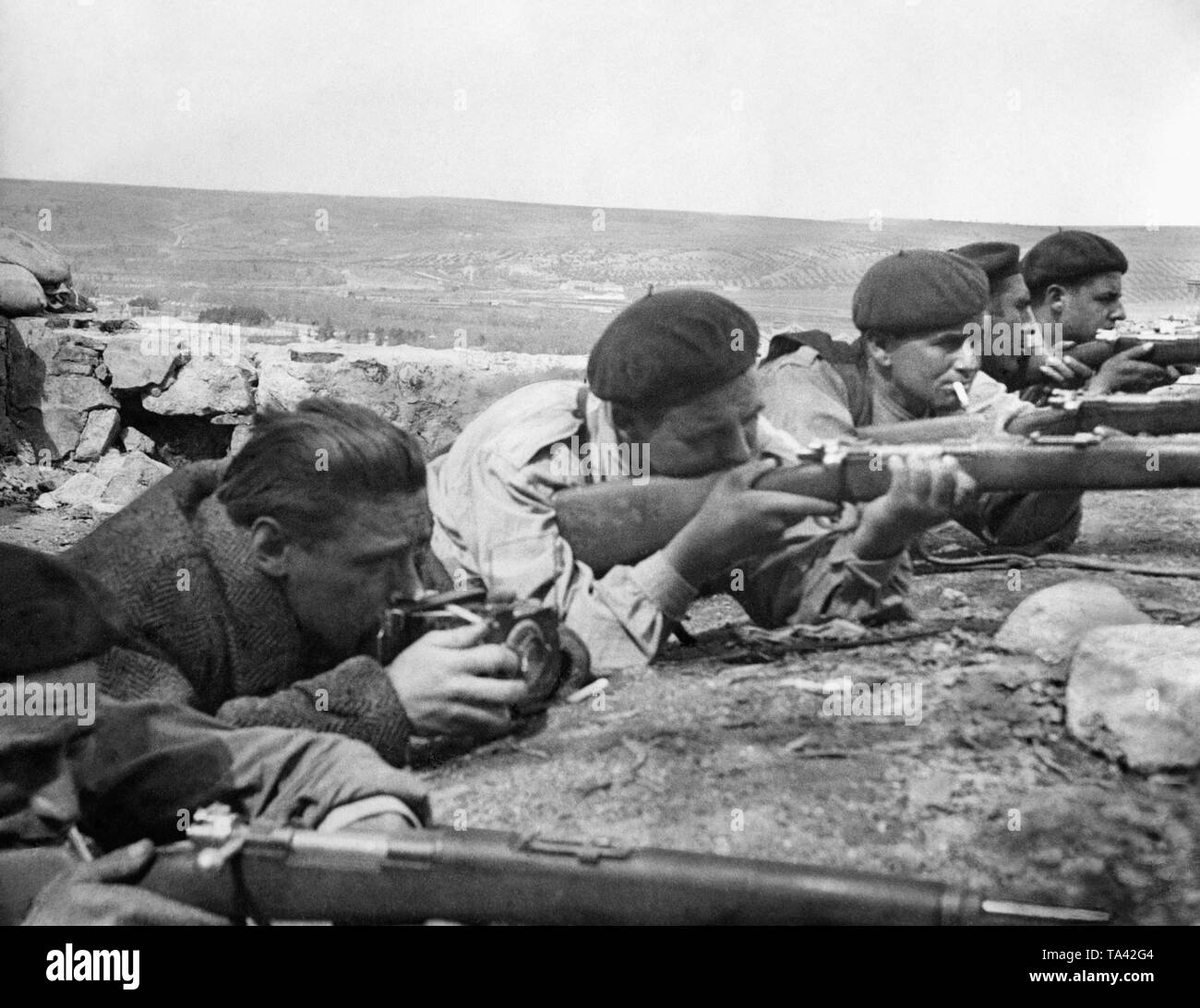 Photo of Republican front fighters in a position at the front during the Spanish Civil War. The fighters have guns at the ready. Second from left, a photographer with camera. Stock Photo