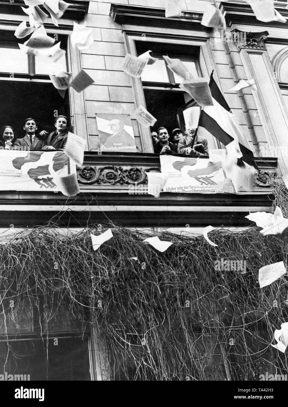 Supporters of the German National People's Party throw flyers out of the windows. On the house front there are two election posters hanging, one of which states 'Vote for German Nationals!',and the other one promotes: 'Down with the International! Vote for German National! ' Stock Photo