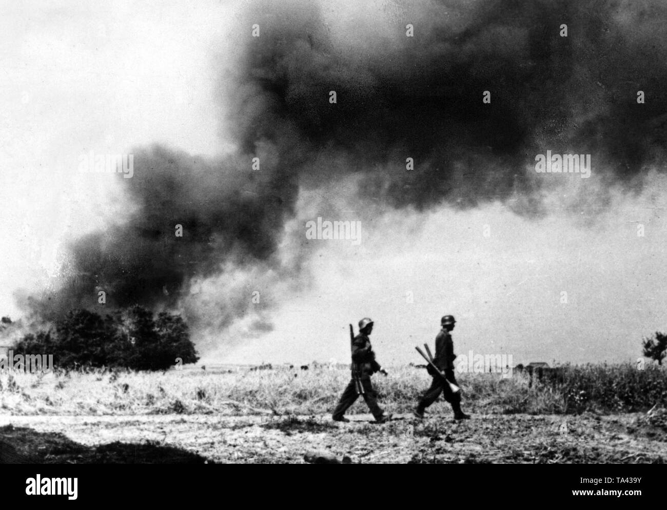 German soldiers cross a field east of the Vistula. In the background, a hut burning by artillery fire. Due to the Operation Bagration of the Red Army, it comes to the collapse of the Army Group Centre in the summer of 1944. Photo of the Propaganda Company (PK): war correspondent Kocherber. Stock Photo